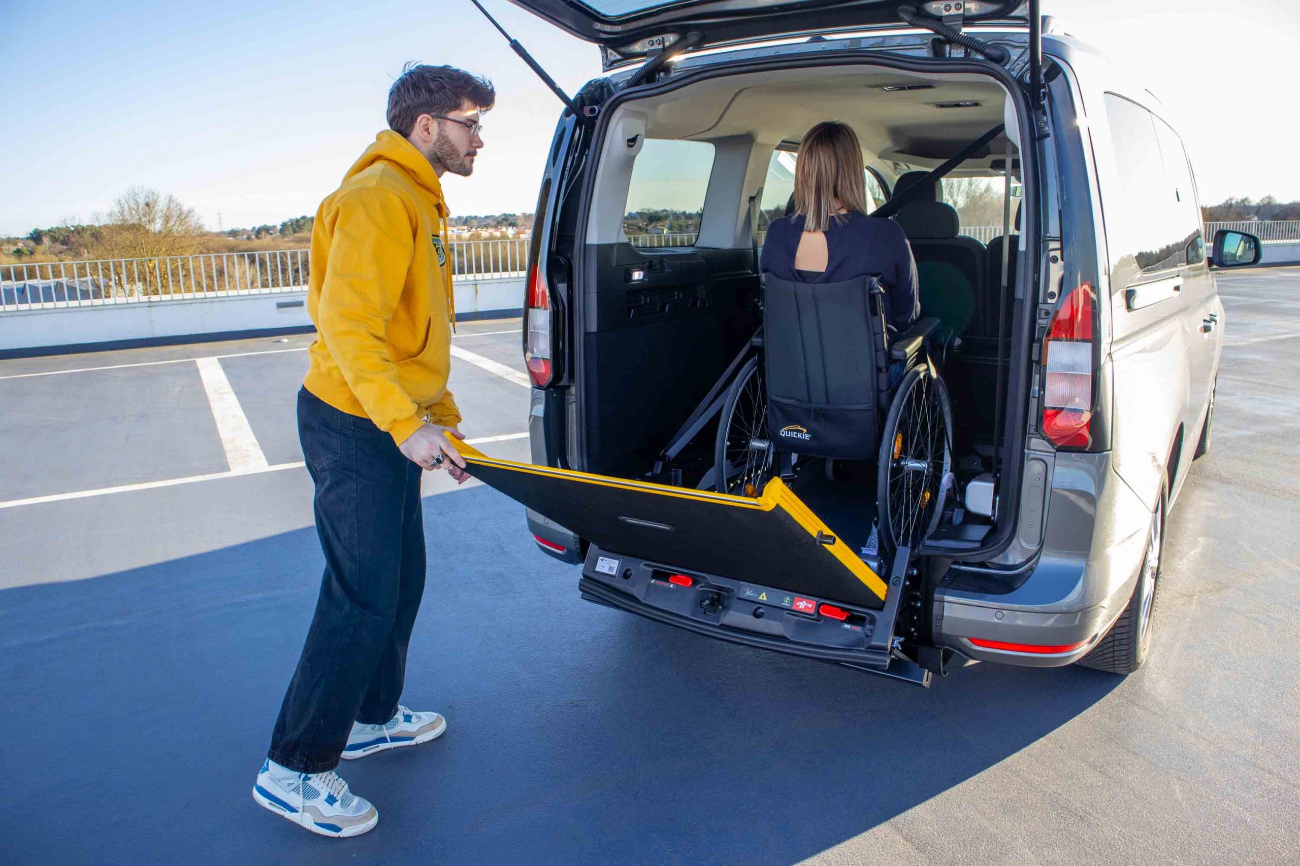 homme déplayant un haillon, femme en fauteuil de dos dans le véhicule